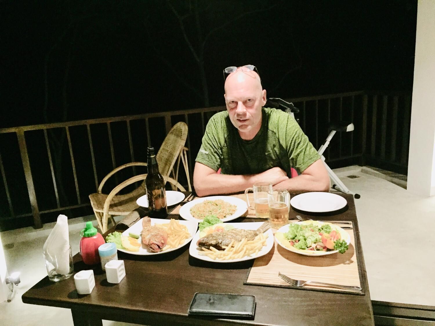 A man seated at a table with plates of food, a bottle, and glasses.