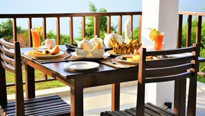 A wooden table set for breakfast with a view of a lake, including plates of fruit, bread, and beverages. - Ashansa Lagoon Resort (Rekawa)