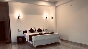 A modern bedroom with a large bed, two wall-mounted lights, a small bedside table, and a wooden floor. - Ashansa Lagoon Resort (Rekawa)