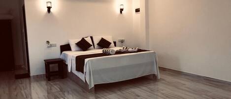 Un dormitorio moderno con una cama grande, dos luces fijadas a la pared, una mesita de noche pequeña y suelo de madera.