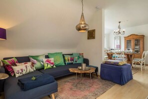 Ein Wohnzimmer mit einem dunkelblauen Sofa, bunten Kissen, einem Holztisch und einem Kronleuchter.