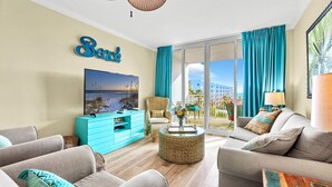 A modern living room with a large TV, teal curtains, and a view of the ocean.