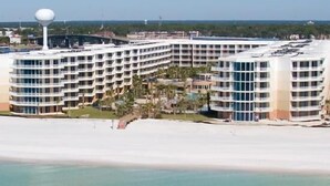 A large, multi-story hotel with a curved facade, located near a beach.