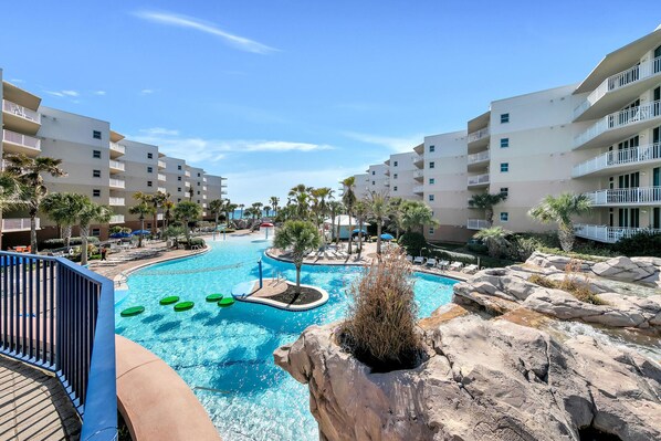 A resort with a central swimming pool, multiple balconies, and palm trees.