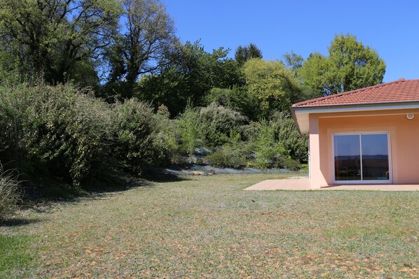 A house with a red-tiled roof, a large sliding glass door, and a grassy yard with trees in the background.