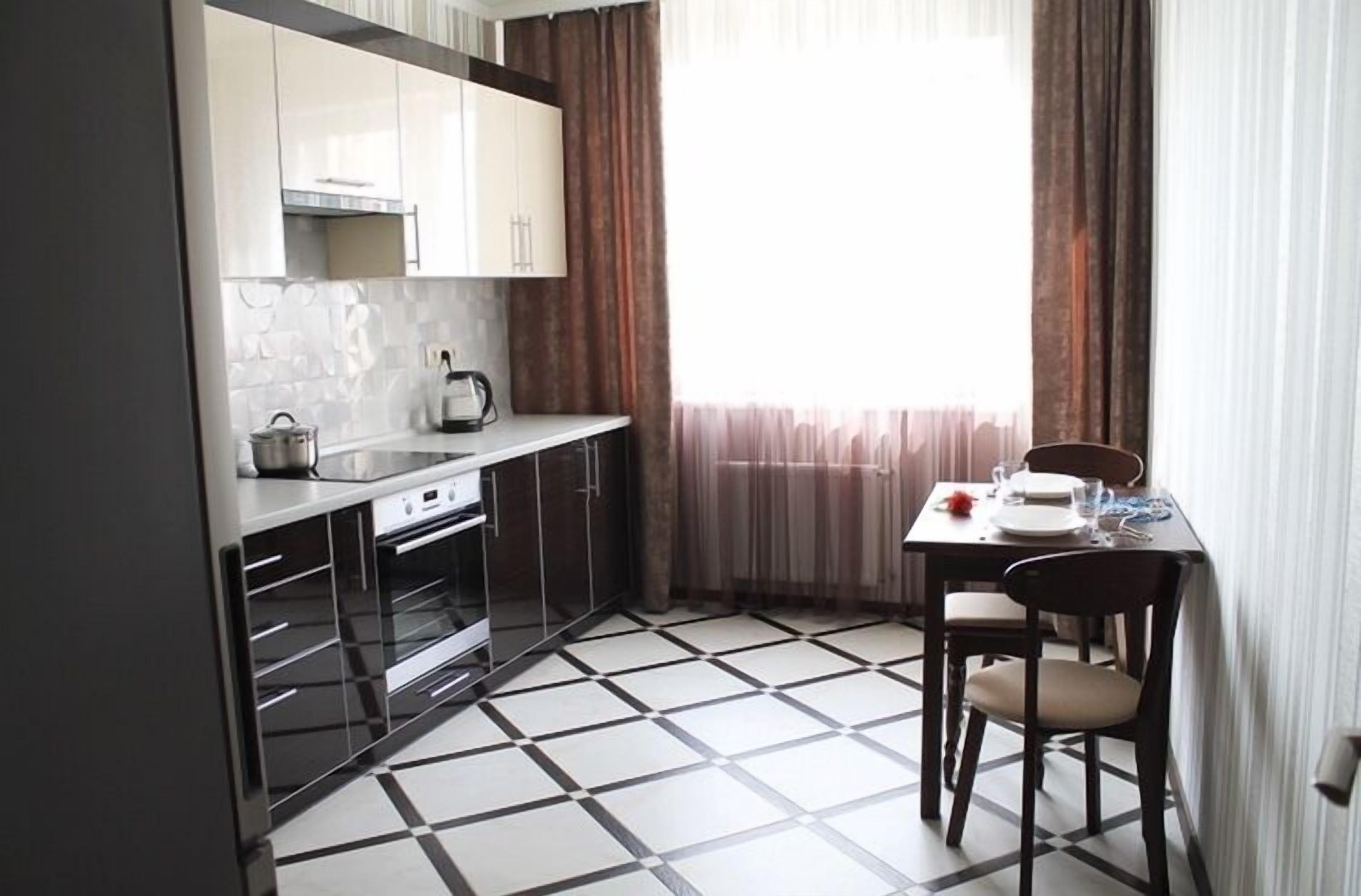 A compact kitchen with a tiled floor, a dining table with chairs, and a window with curtains.