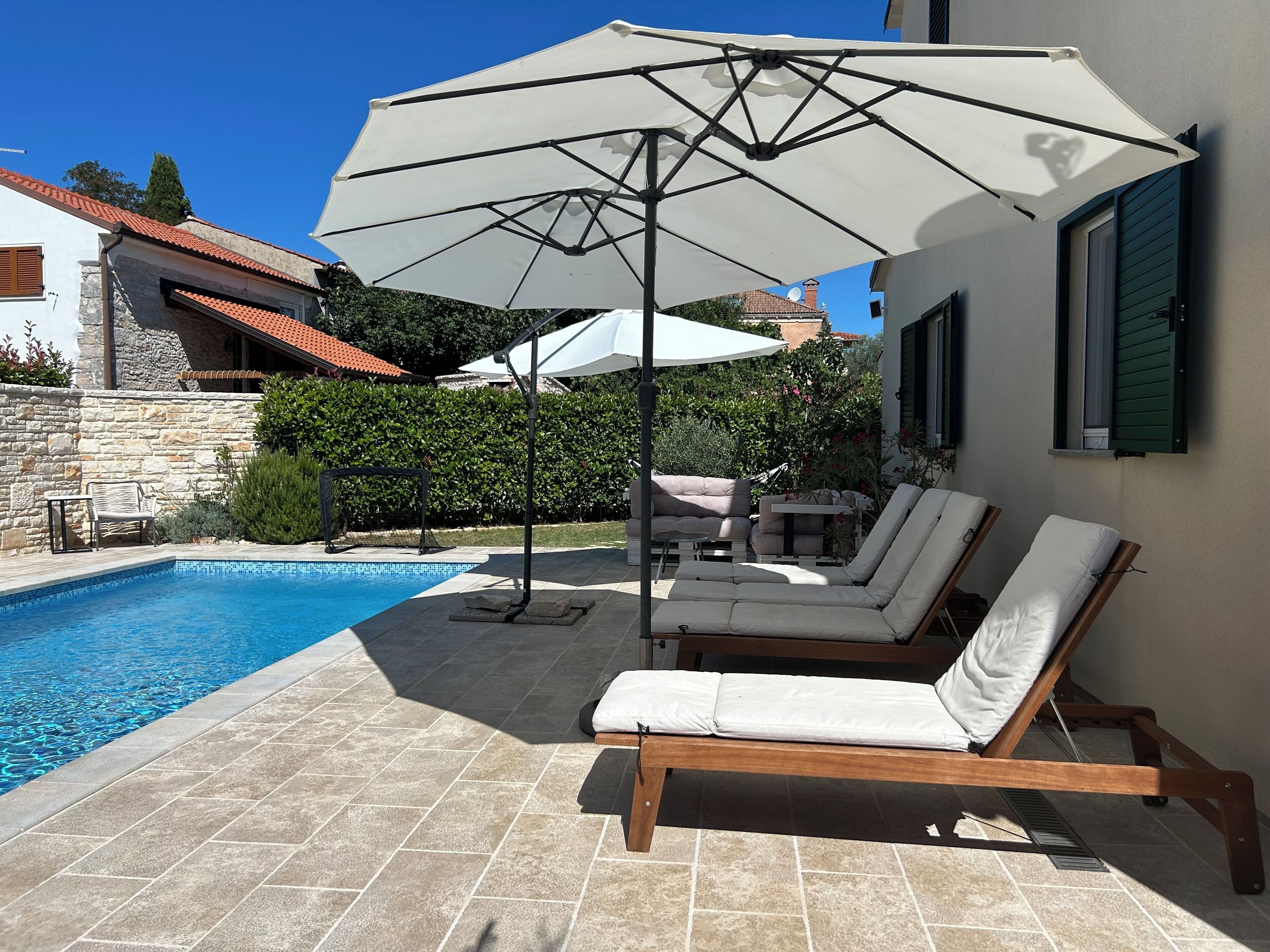 Zona junto a la piscina con piscina, sillas de descanso y sombrillas.