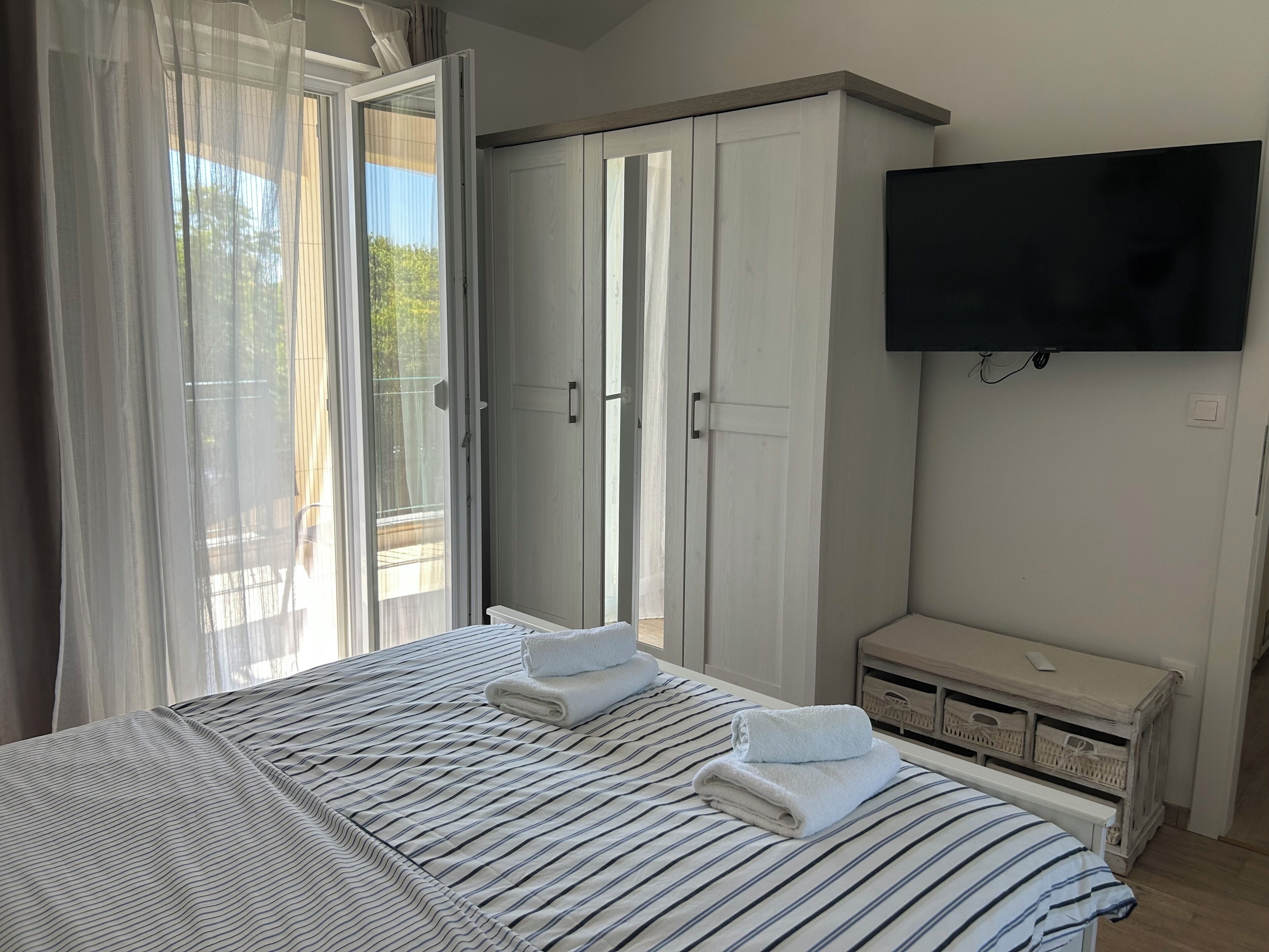 A bedroom with a bed, a TV, a wardrobe, and a window with curtains.