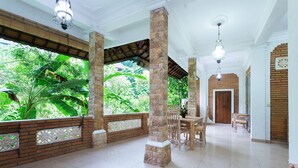 Amplio espacio interior con vistas a exuberante vegetación a través de grandes ventanales, suelo de baldosas y mobiliario de madera.