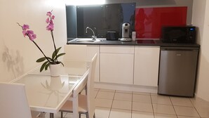 Une cuisine moderne avec une table blanche, une orchidée en pot, une machine à café, un four à micro-ondes et un réfrigérateur.