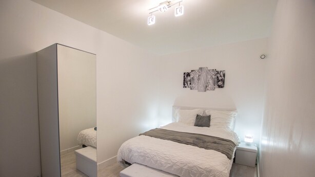 Une chambre à coucher moderne avec un lit, une table de chevet, une commode et un grand miroir.