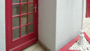 Une porte à cadre rouge, adossée à un mur blanc, et ornée d’un élément décoratif mural.