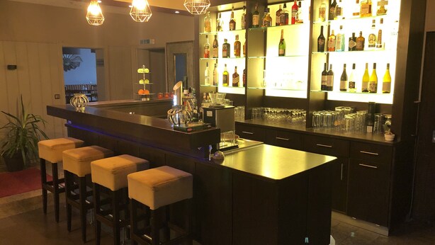 Een bar met een lange toonbank, krukken en diverse flessen en glazen.