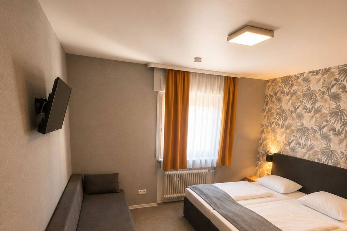 A hotel room with a bed, a desk, a chair, a TV, and a window with curtains.