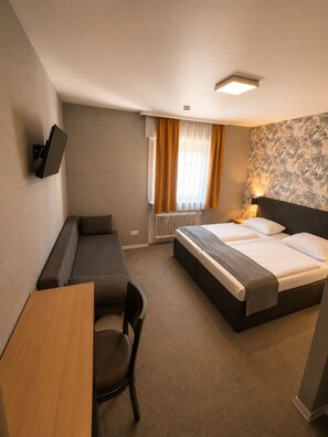 Een hotelkamer met een bed, een bureau, een stoel, een televisie en een raam met gordijnen.