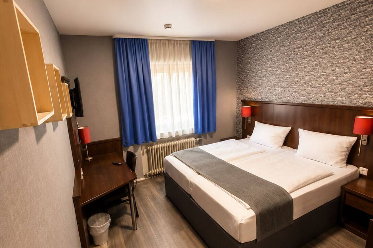 A hotel room with a large bed, a desk, a chair, a TV, and a stone wall.