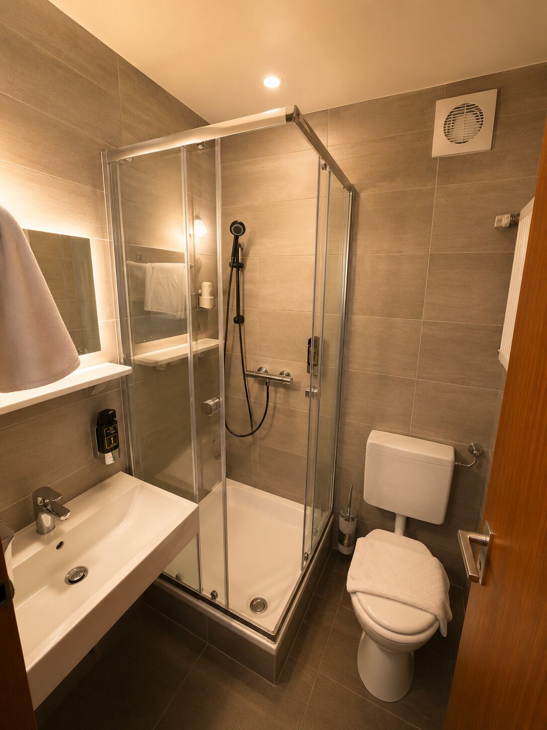 Moderni kylpyhuone, jossa on lasiseinällä varustettu suihku, valkoinen pesuallas ja wc.