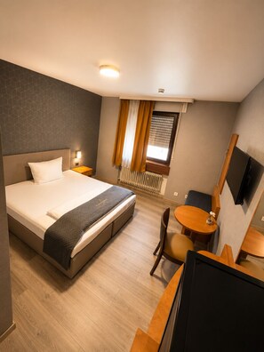 A hotel room with a bed, bedside table, chair, desk, and a TV. - Parkhotel Lindenhof (Offenbach am Main)