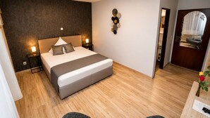 Een moderne hotelkamer met een groot bed, nachtkastjes, een decoratief wandobject en uitzicht naar buiten door een deur.
