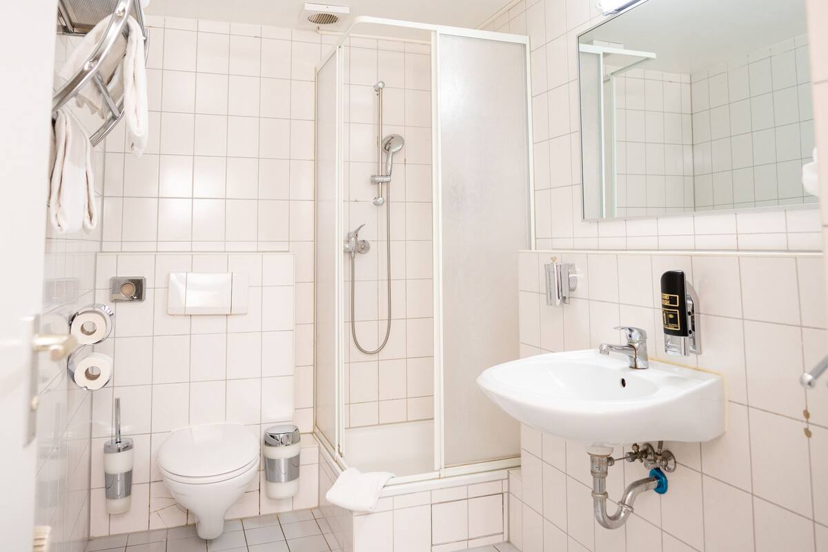 A bathroom with a toilet, sink, shower, and towel rack.