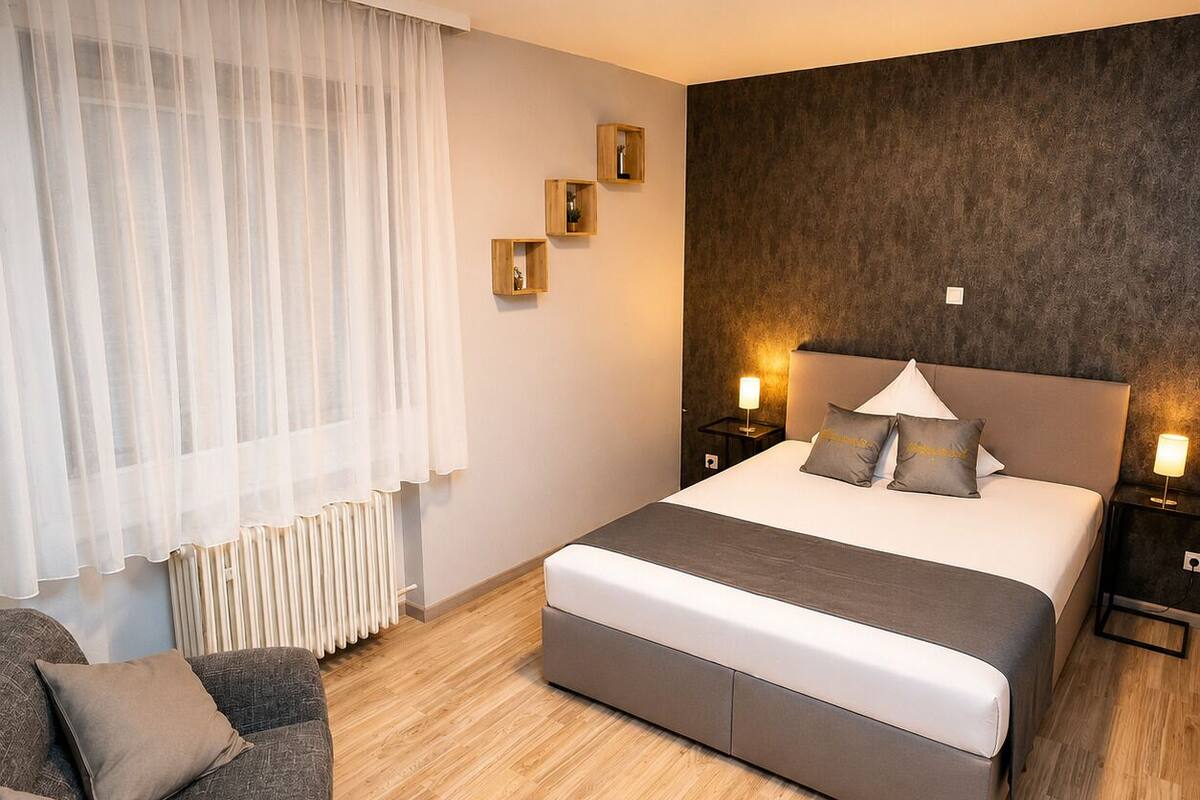 A modern bedroom with a large bed, bedside tables, a sofa, and a radiator.