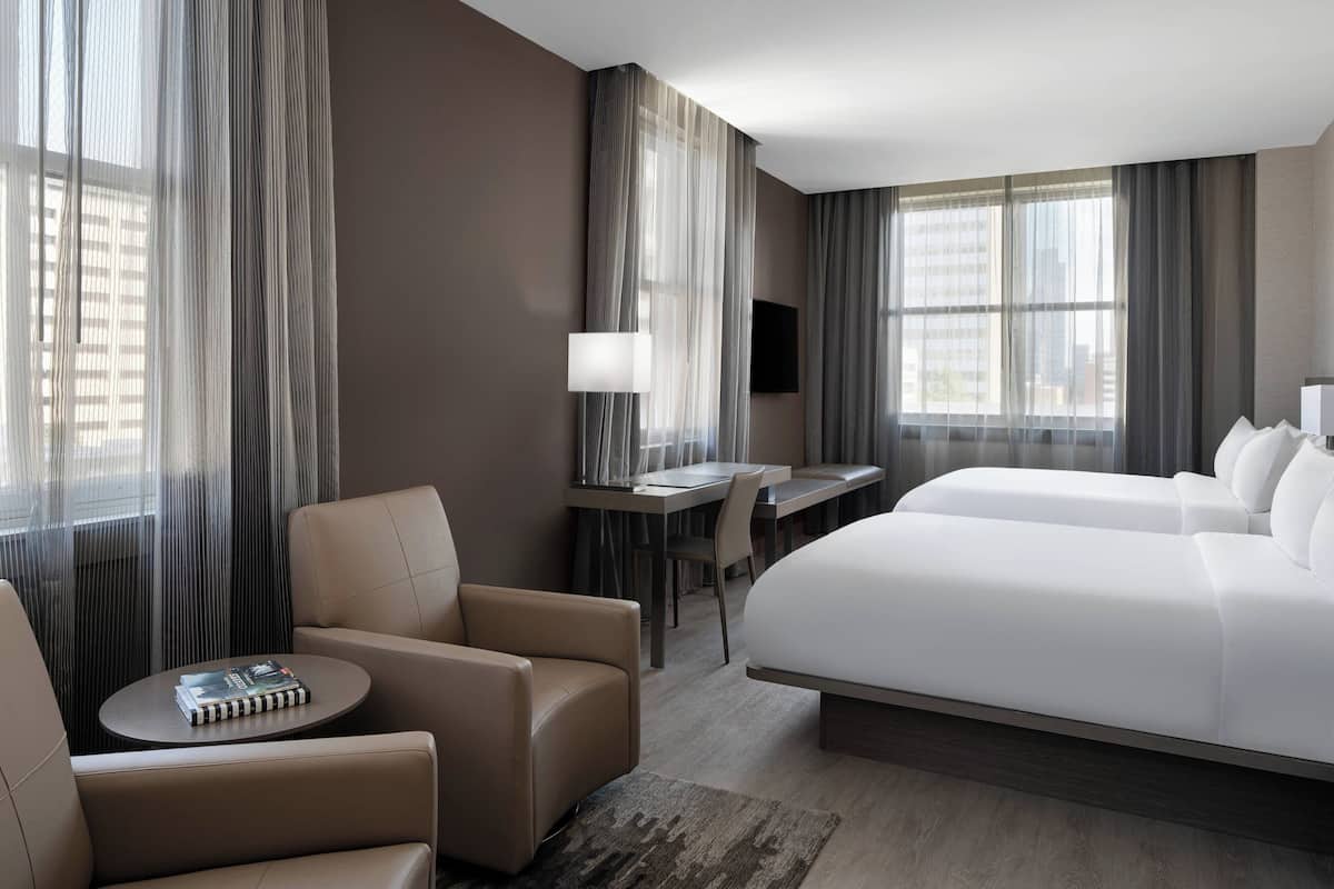Una habitación de hotel con cama, dos sillones, un escritorio y televisión.