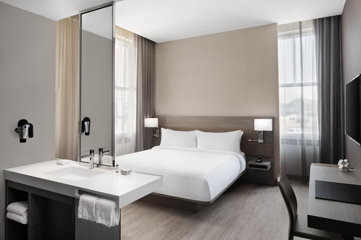 Habitación de hotel moderna con una cama grande, un escritorio independiente, una tocador con espejo y un televisor de pantalla plana.
