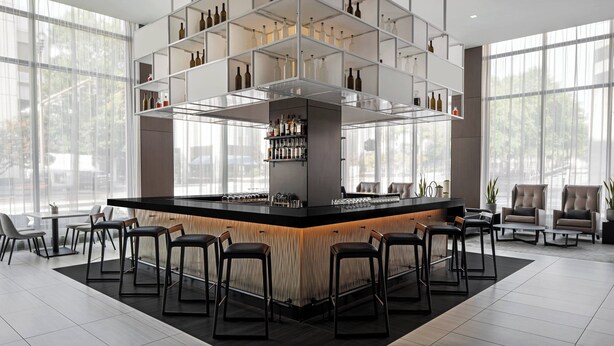 Zona de bar moderna con una barra central, varios estantes para botellas y asientos alrededor.