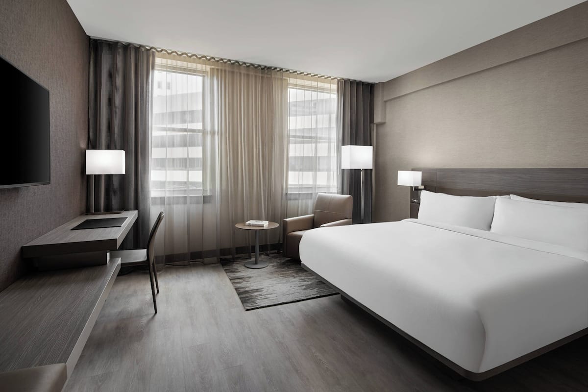 Una habitación de hotel moderna con una cama grande, un escritorio, dos sillas, una mesita y un televisor.