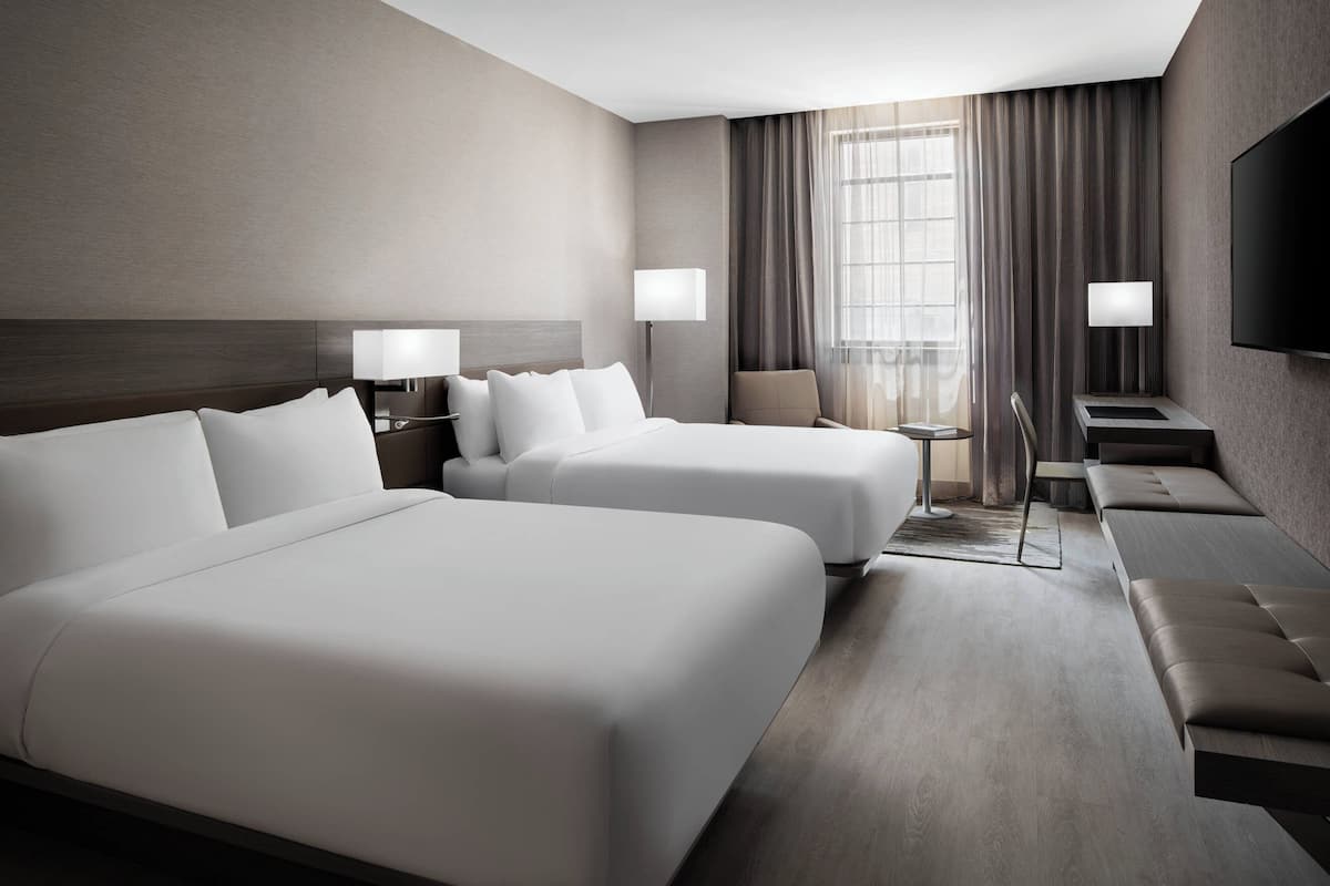 Habitación de hotel con dos camas grandes, un sofá, un televisor y una pequeña mesa.