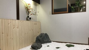 A minimalist indoor garden with a wooden bench, white pebbles, rocks, and a small water feature. - Osaka Premium House (Osaka)