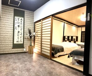 Una habitación tradicional japonesa con suelo de tatami, un fusuma y una cama con colcha blanca, además de un jarrón con flores.