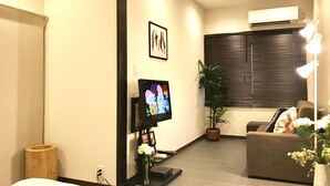 A living room with a flat-screen TV, a potted plant, a sofa, and a wall-mounted air conditioner. - Osaka Premium House (Osaka)