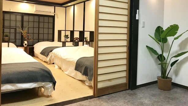 A room with two beds, a sliding shoji screen, a potted plant, and a wall-mounted light fixture. - Osaka Premium House (Osaka)