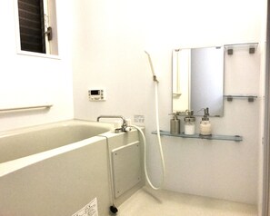A bathroom with a bathtub, a handheld showerhead, a sink with a mirror, and shelves with toiletries. - Osaka Premium House (Osaka)