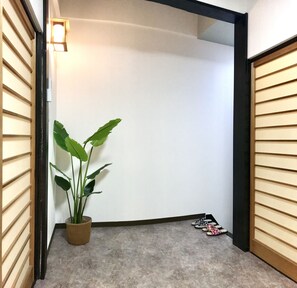 A hallway with a potted plant, a pair of slippers, and a door with a light fixture. - Osaka Premium House (Osaka)