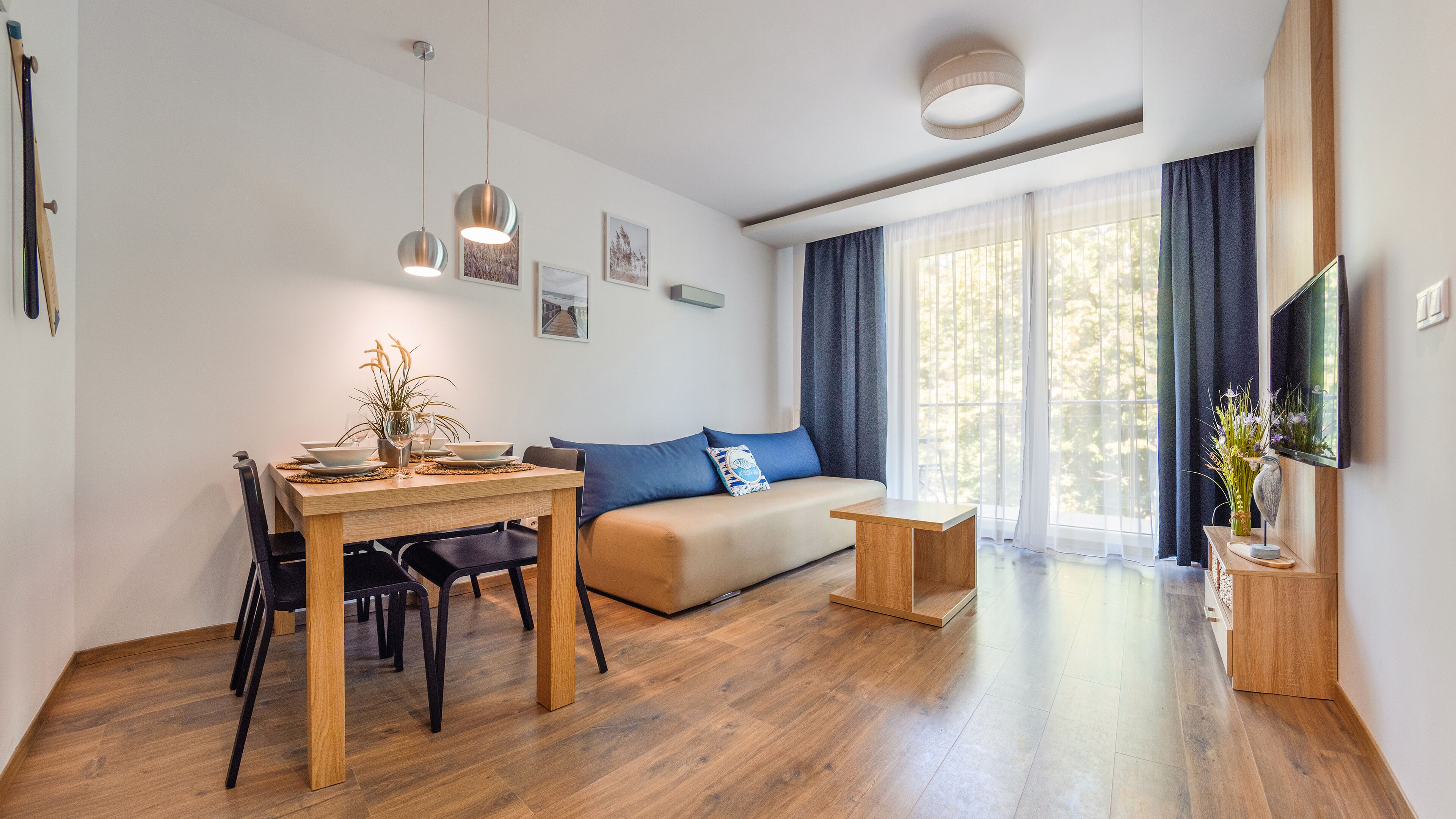 Ein modernes Wohnzimmer mit einem Holzesstisch, einer Couch und einem an der Wand montierten Fernseher.