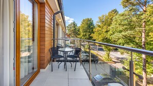 A balcony with a table and chairs, overlooking a parking area and trees.