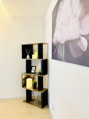 Een hoek van een kamer met een zwarte en gouden wandplank, met kaarsen, een lijst met foto en een kleine plant.