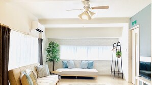 A modern living room with a sofa, a round rug, a standing plant, and a TV. - Shioji Aoi Villa (Osaka)