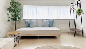 A bedroom with a bed, a small round table, a hanging plant, and a window with curtains. - Shioji Aoi Villa (Osaka)