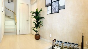 A hallway with a staircase, a potted plant, and a shoe rack. - Shioji Aoi Villa (Osaka)