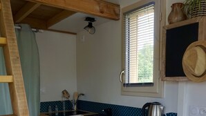 A compact kitchen with white cabinets, a wooden countertop, a kettle, and a window with blinds.