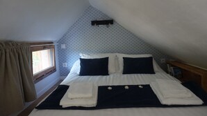 A neatly made bed with white and dark blue linens, a small bedside table with a book, and a window with curtains.