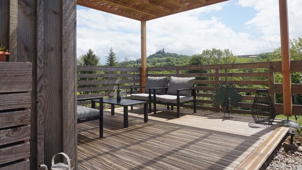 A wooden deck with a pergola, outdoor furniture, and a view of a green landscape.