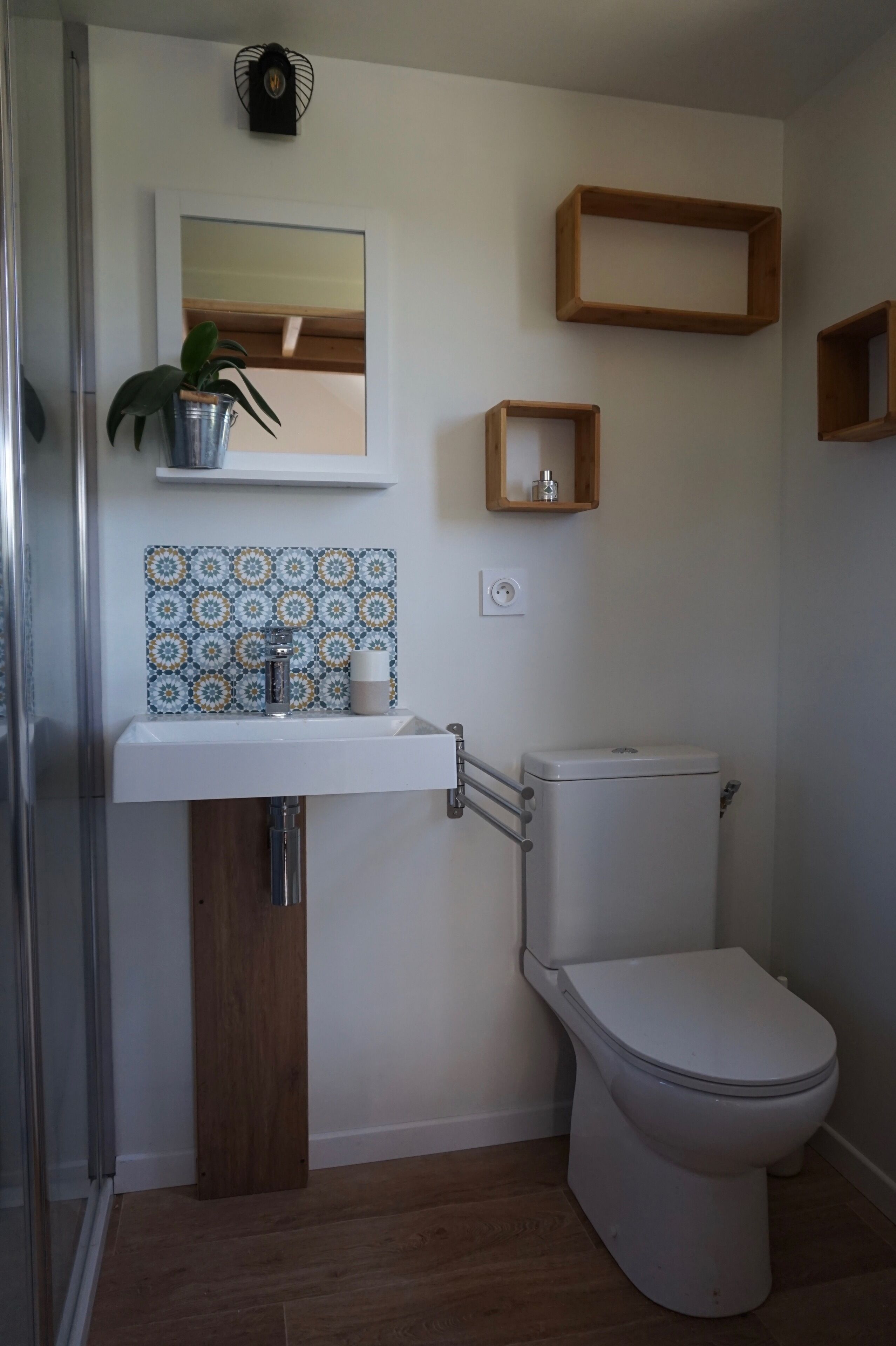 Un baño con lavamanos blanco, inodoro, espejo y una planta en maceta.