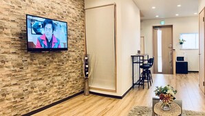 A modern hotel lobby with a stone wall, a flat-screen TV, a dining area, and a reception desk. - Asahi Kasumi Villa (Osaka)