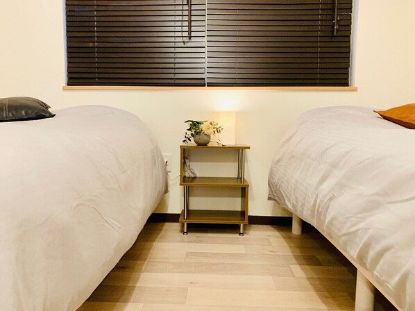 Un dormitorio con dos camas, una mesita de noche con lámpara y una ventana con persianas.