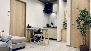 A compact living space with a kitchenette, a dining area with a foldable table and chairs, a sofa, and a potted plant. - Hanazonominami Apartment 101 (Osaka)