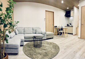 A modern living room with a grey sectional sofa, a round coffee table, and a potted plant. - Hanazonominami Apartment 101 (Osaka)